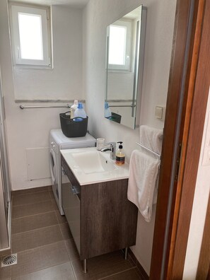 Ein kleines Badezimmer mit Waschmaschine, Waschbecken, Spiegel und Handtuchhalter.