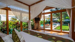 Quarto com cama grande, televisão e vista para a piscina e jardim.