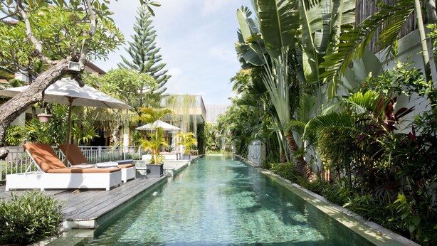 Área de piscina com espreguiçadeiras e guarda-sóis, rodeada por vegetação tropical exuberante.