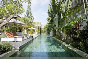 A pool area with lounge chairs and umbrellas, surrounded by lush tropical plants.