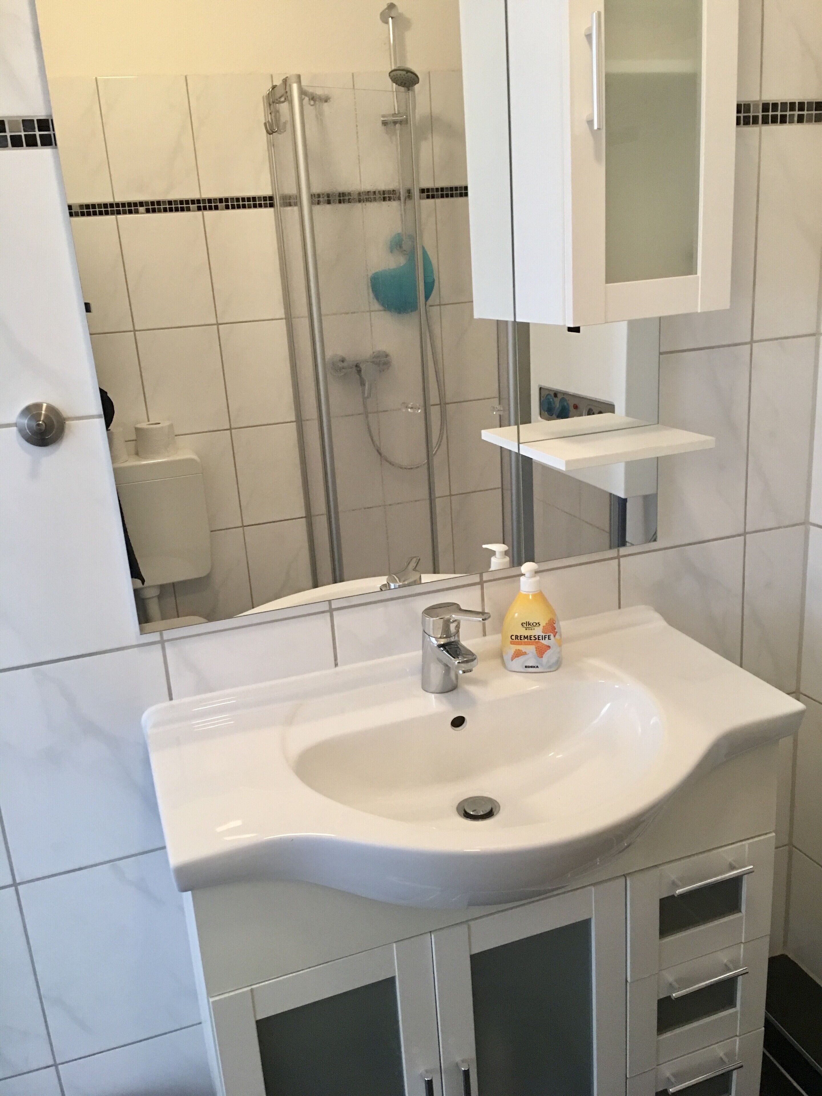 A bathroom with a white sink, a mirror above it, and a shower area with a blue showerhead.