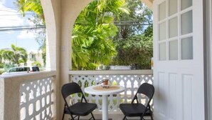 A balcony with two chairs and a small table, surrounded by a white fence and lush greenery. - Cozy 2-Bedrooms across from West Coast beach (St James)