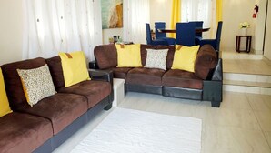 A living room with a sectional sofa, a white rug, and a painting on the wall. - Cozy 2-Bedrooms across from West Coast beach (St James)
