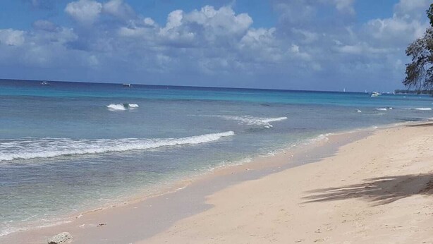A beach with clear turquoise water, a sandy shore, and a few boats in the distance. - Cozy 2-Bedrooms across from West Coast beach (St James)