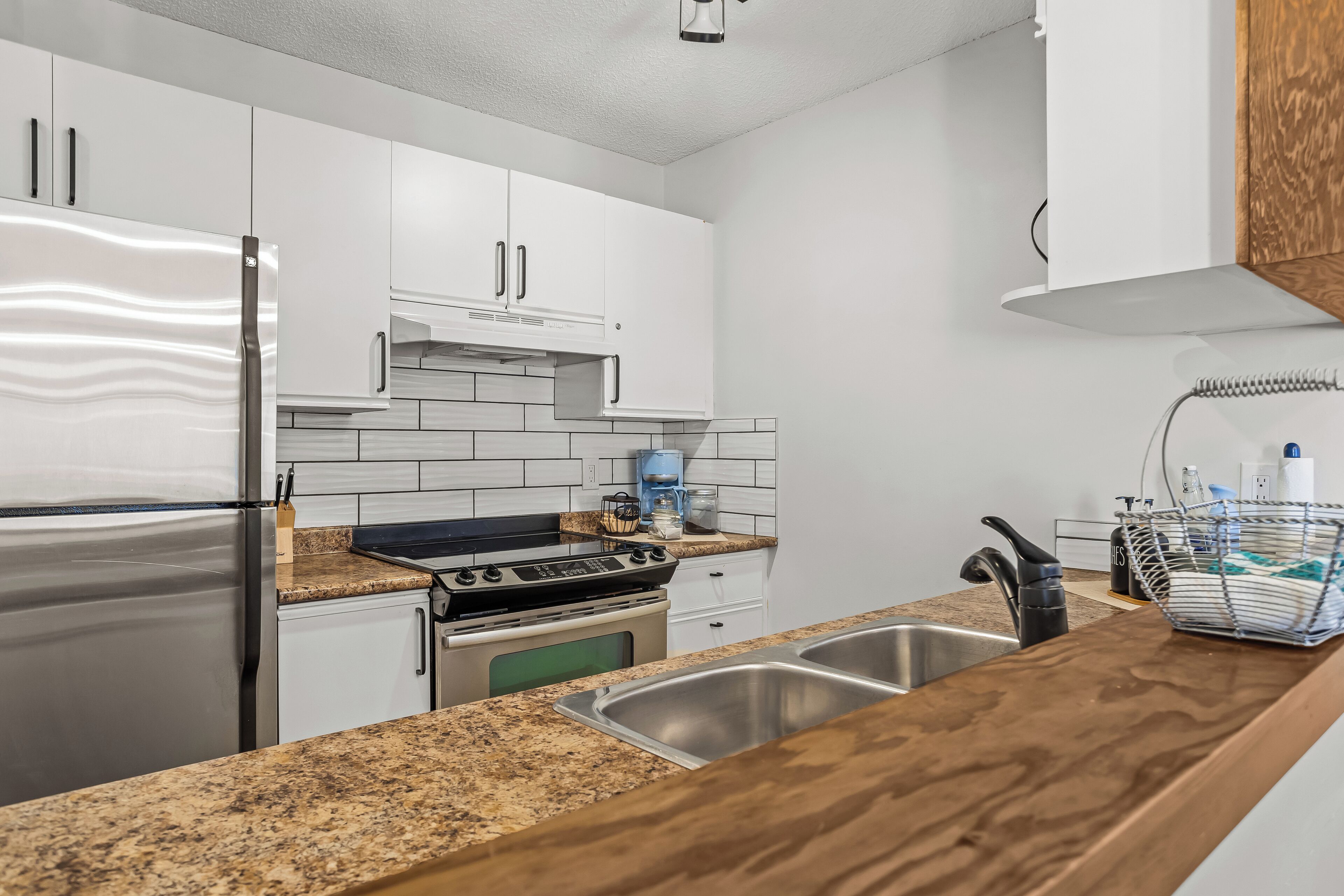 Una cocina moderna con armarios blancos, un refrigerador de acero inoxidable, una estufa a gas y un lavaplatos doble.