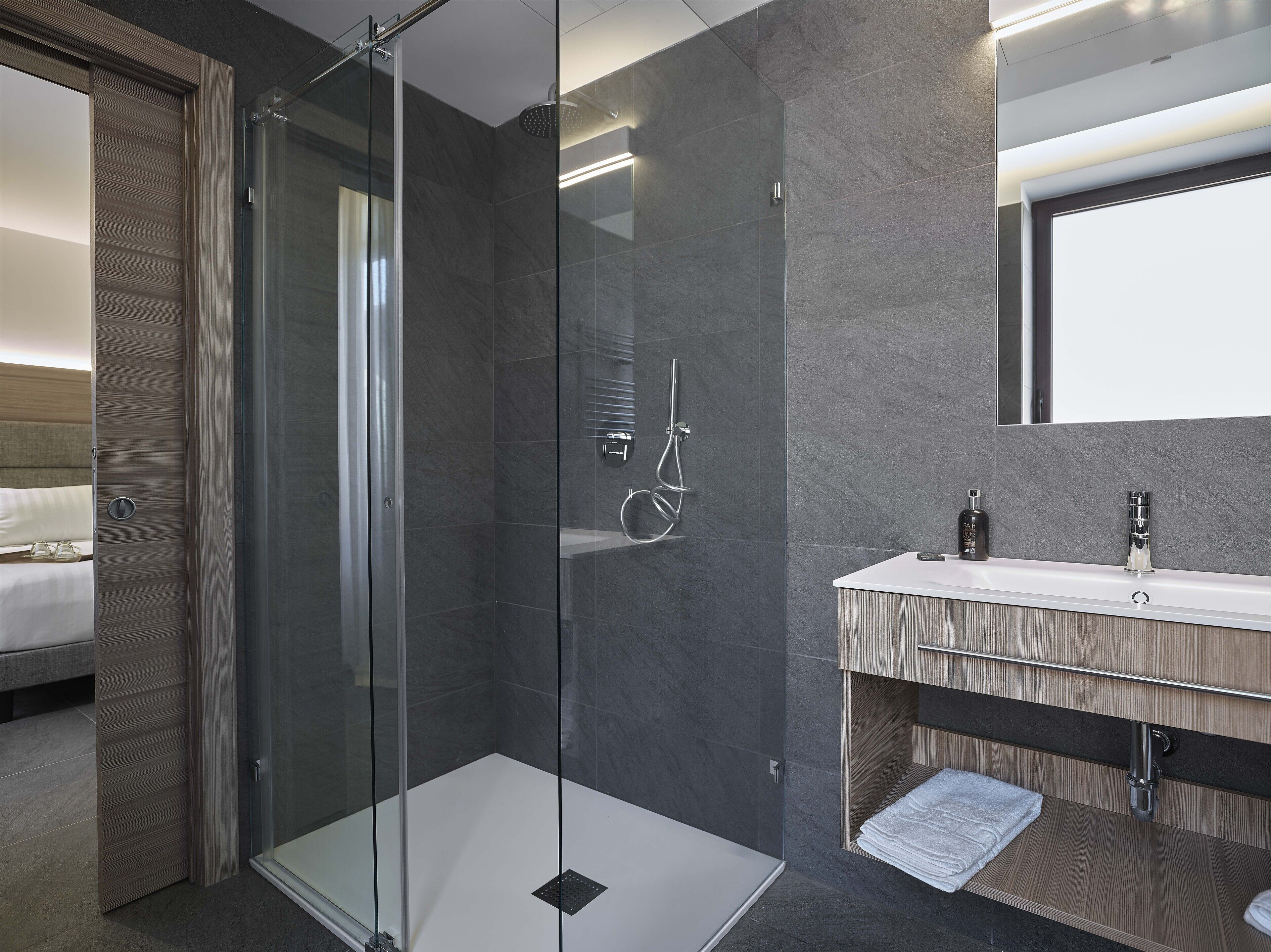 Un baño moderno con ducha envuelta en vidrio, tocador de madera y un espejo grande.