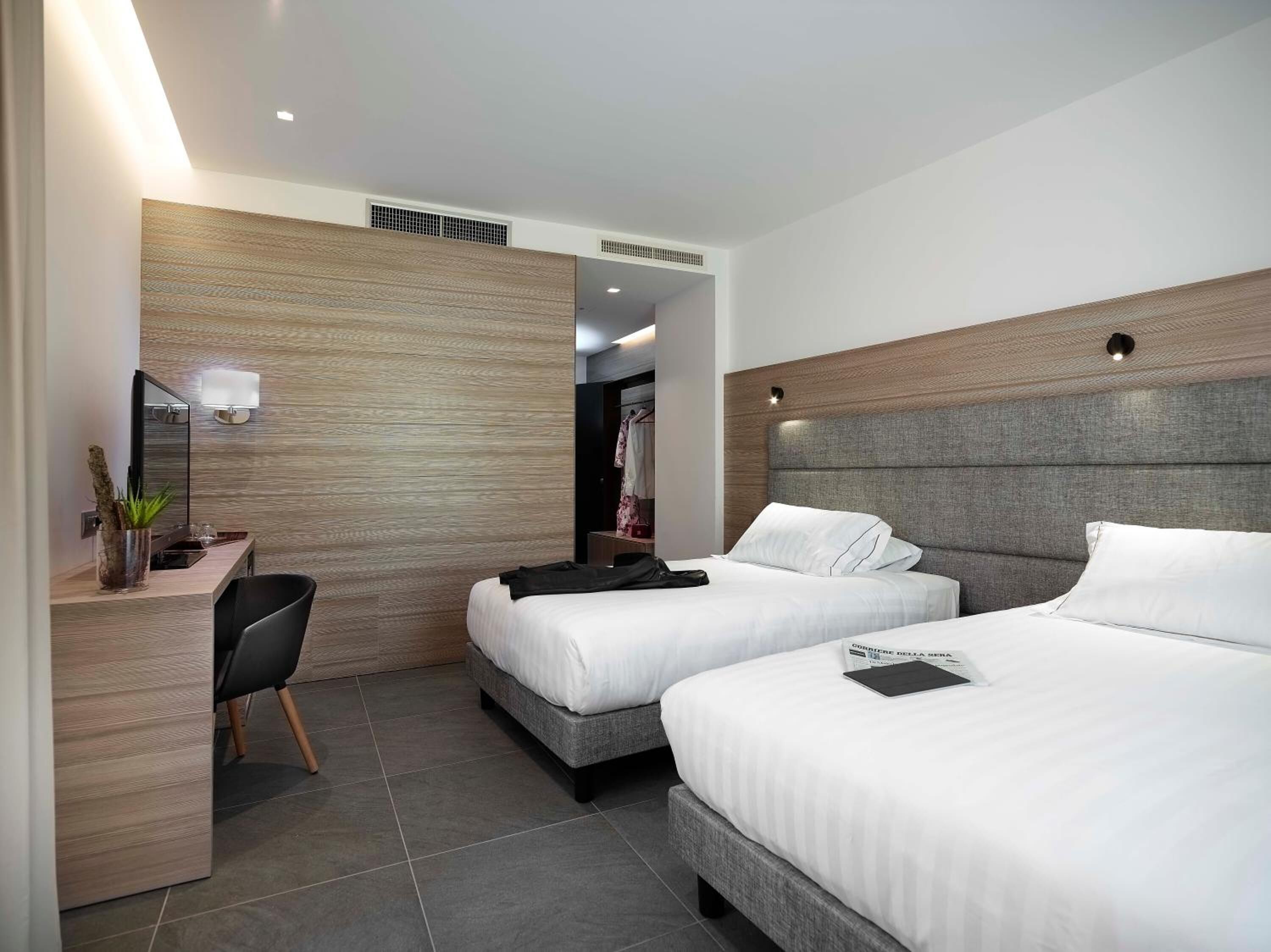 A modern hotel room with two beds, a desk, and a chair.