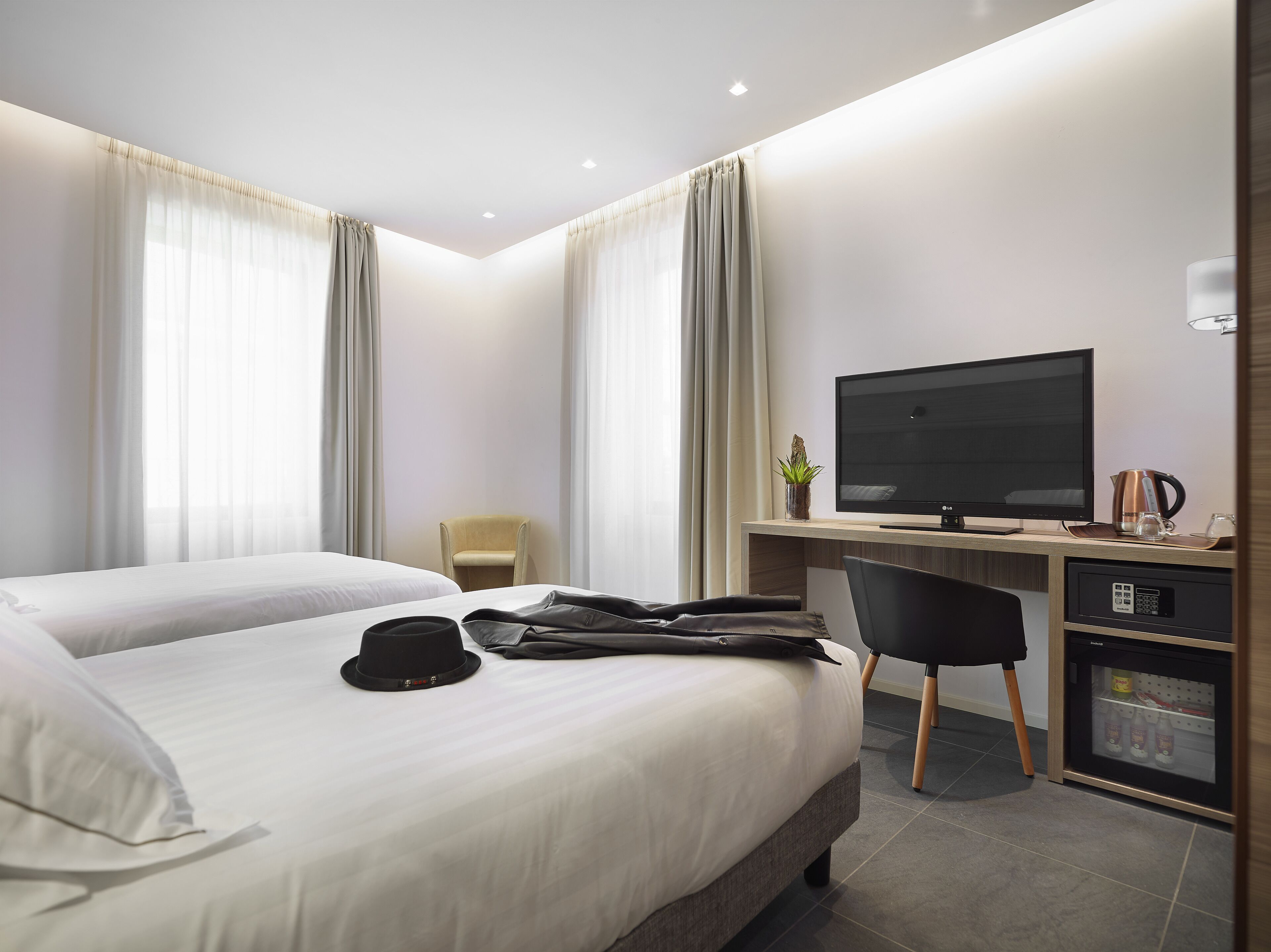 A hotel room with two beds, a desk with a television, a chair, and a minibar.