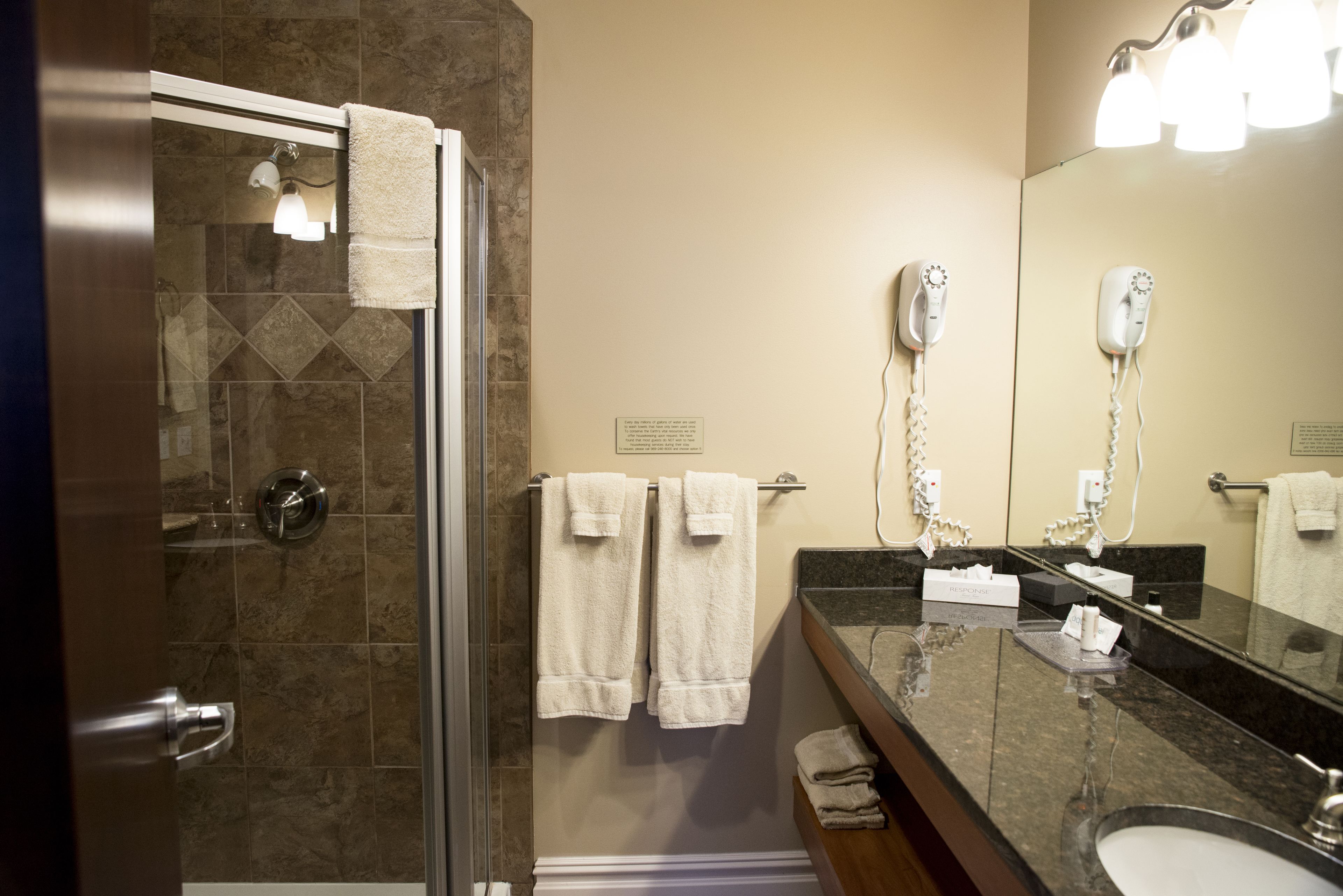 A bathroom with a glass shower door, a sink with a mirror, and two hair dryers mounted on the wall.