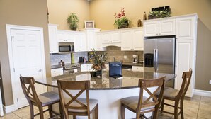 A kitchen with white cabinets, a large island with bar stools, a refrigerator, and a microwave. - Riverwalk Place Resort & Spa (Gladwin)