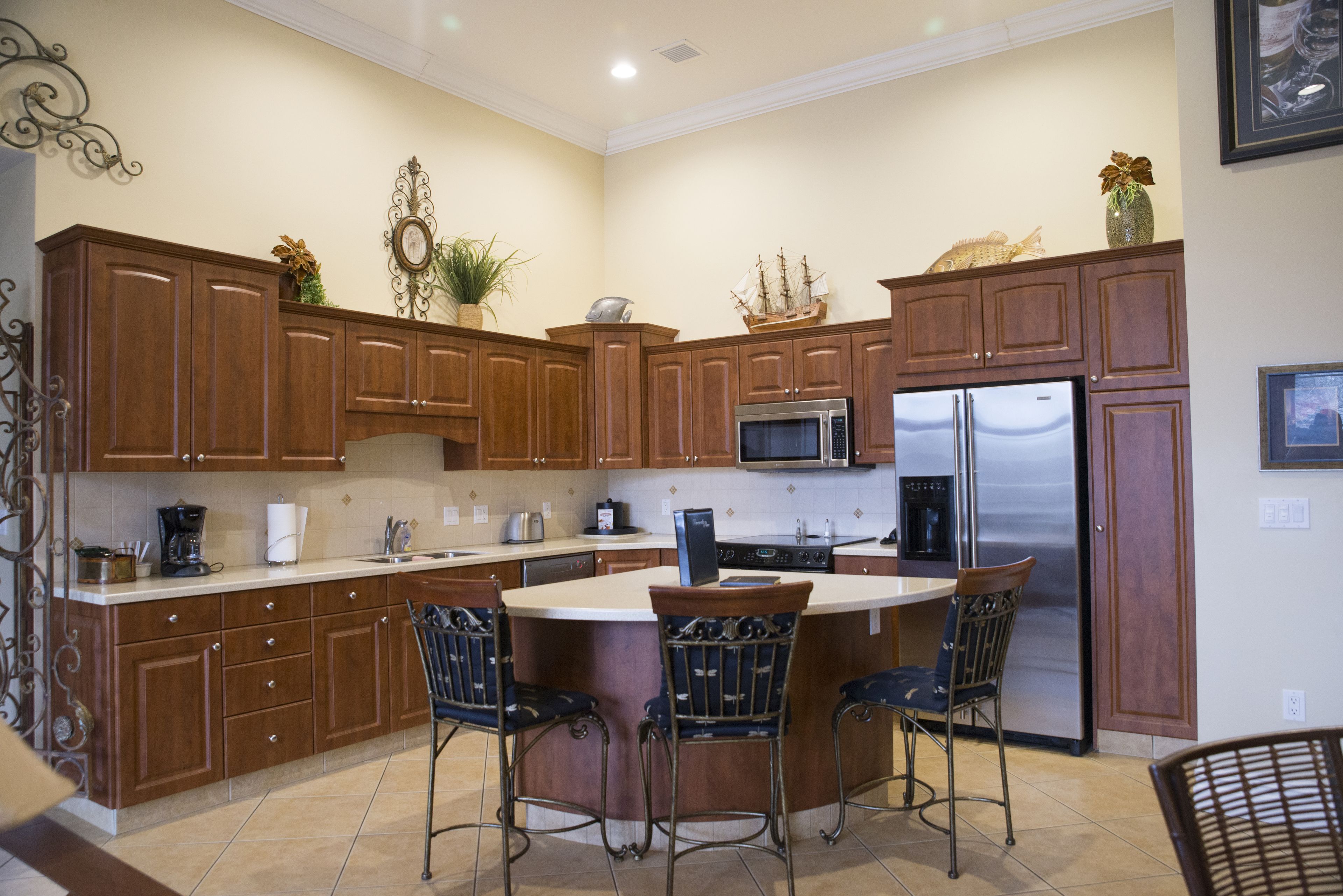 Una cocina con armarios de madera, una isla central con sillas, un refrigerador y un microondas.