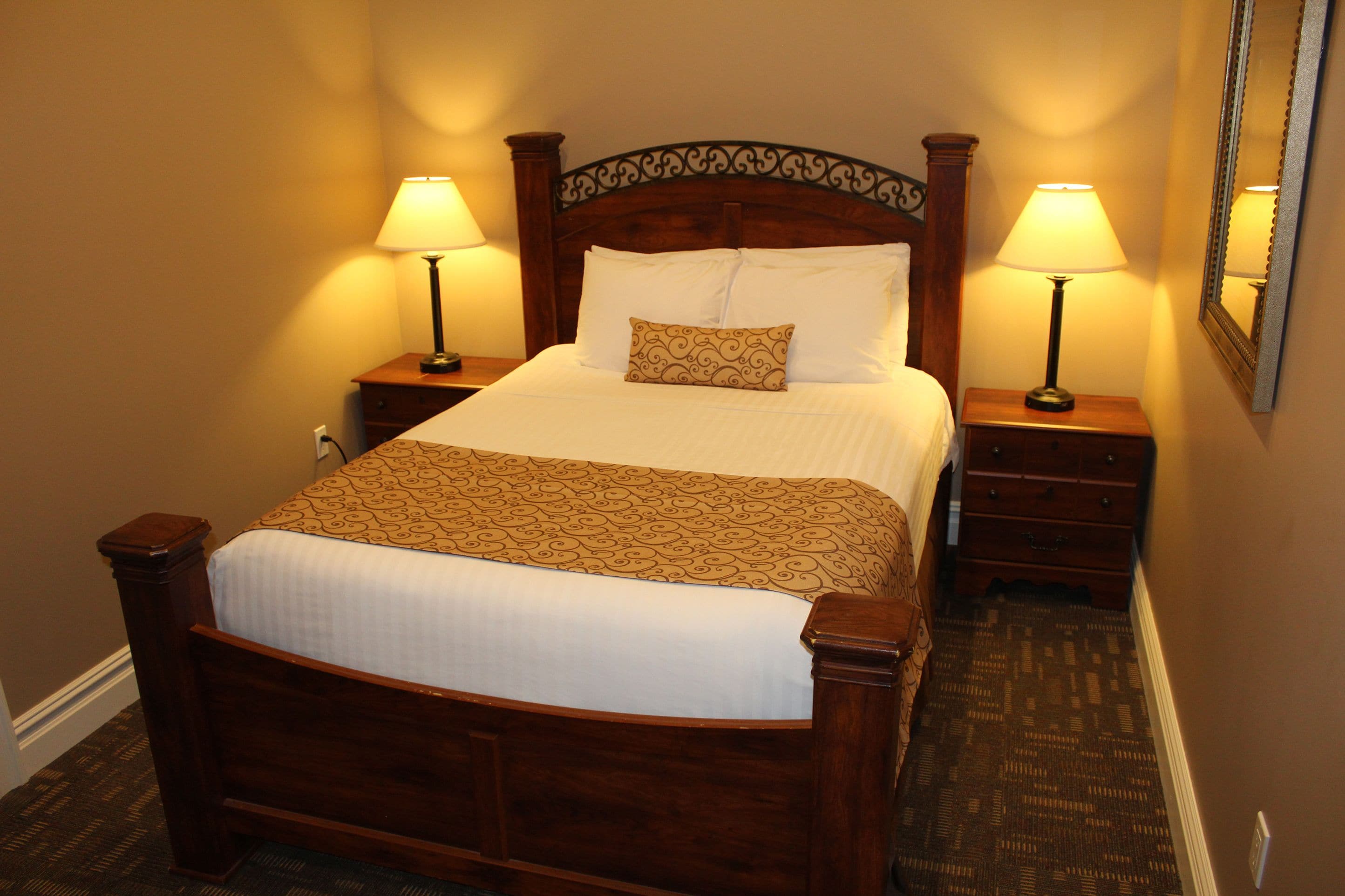 A neatly made bed with a patterned bedspread, two bedside lamps, and a wooden headboard.