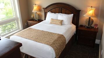 Una cama bien tendida con una colcha estampada, dos lámparas de noche y una mesita con un objeto decorativo.