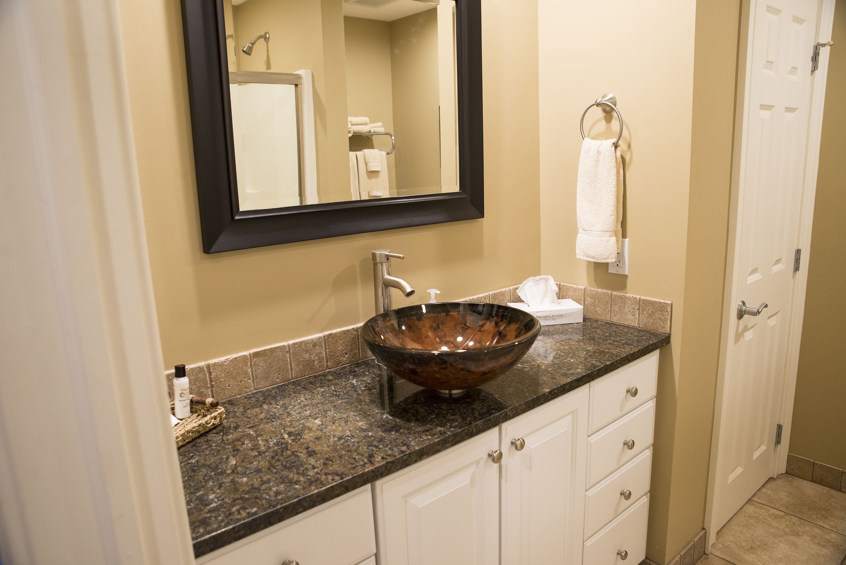A bathroom with a large mirror, a vessel sink, a towel rack, and a door.