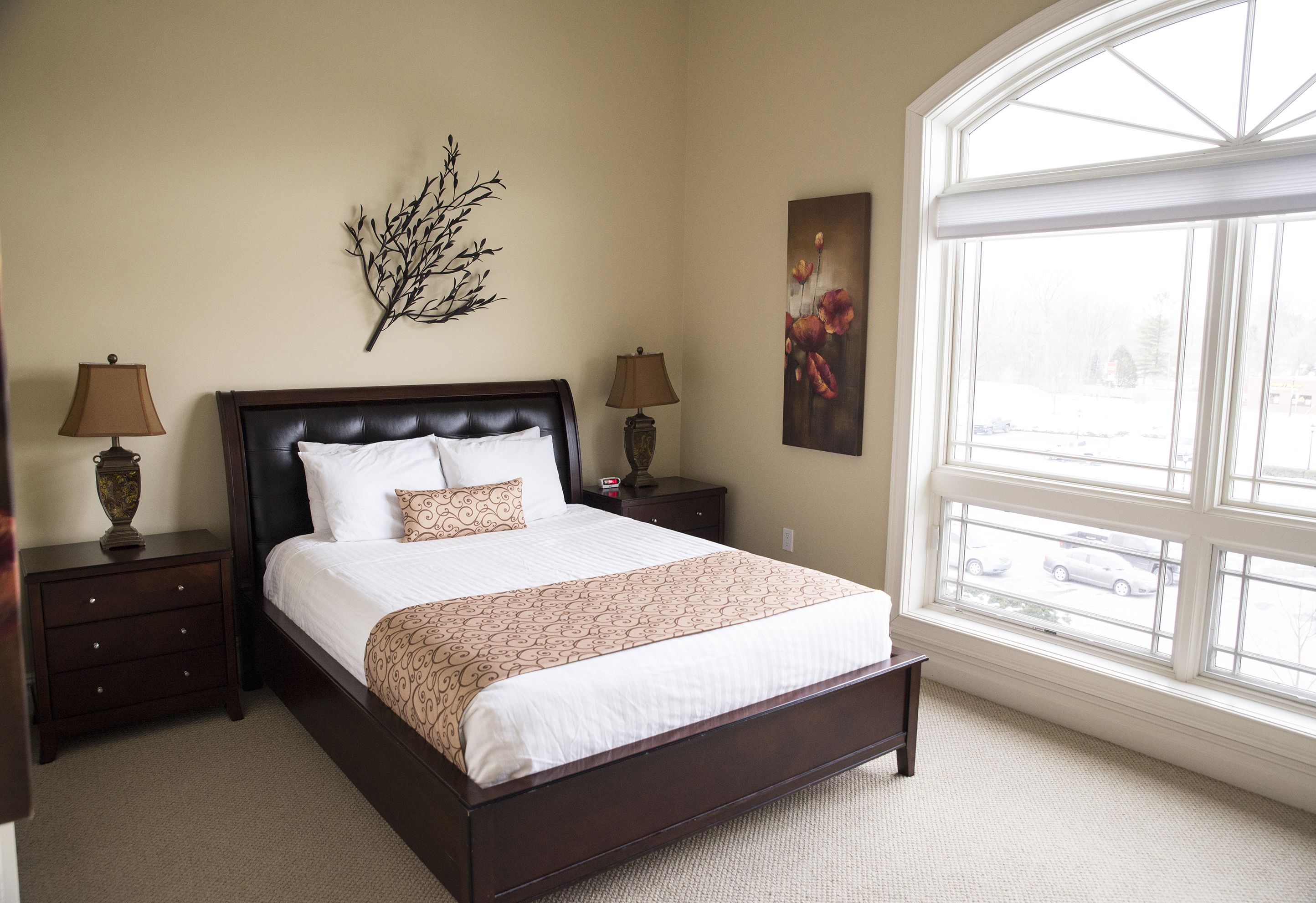 A bedroom with a large bed, two nightstands, a window with a view, and wall art.