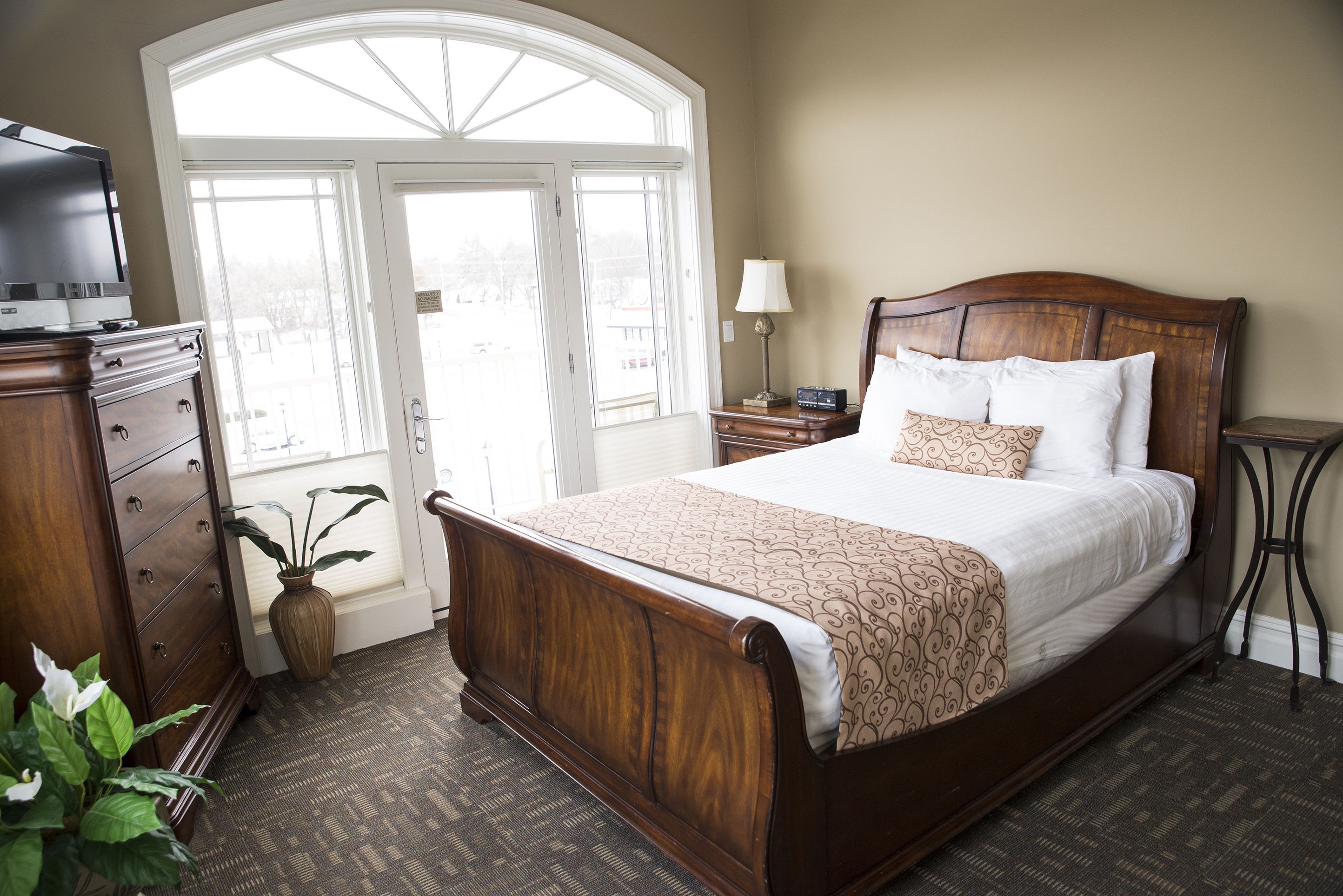 A bedroom with a large bed, a dresser, a lamp, and a potted plant.