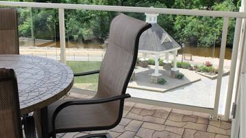 A balcony with a table and chairs, overlooking a river and a gazebo.