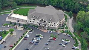 A large building with a parking lot, surrounded by greenery and a river. - Riverwalk Place Resort & Spa (Gladwin)