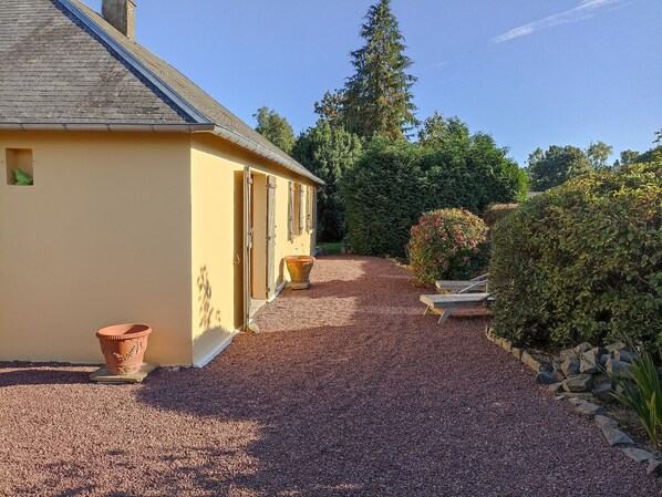 A yellow building with a gravel driveway and a wooden bench.