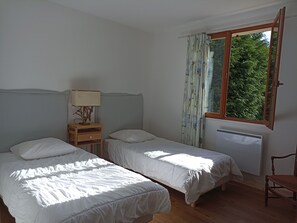 A bedroom with two single beds, a bedside table with a lamp, a window with curtains, and a radiator.