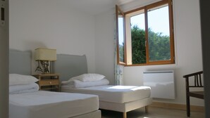 Ein Schlafzimmer mit zwei Einzelbetten, einem Nachttisch mit Lampe, einem Fenster mit Blick auf Bäume und einer Heizung.