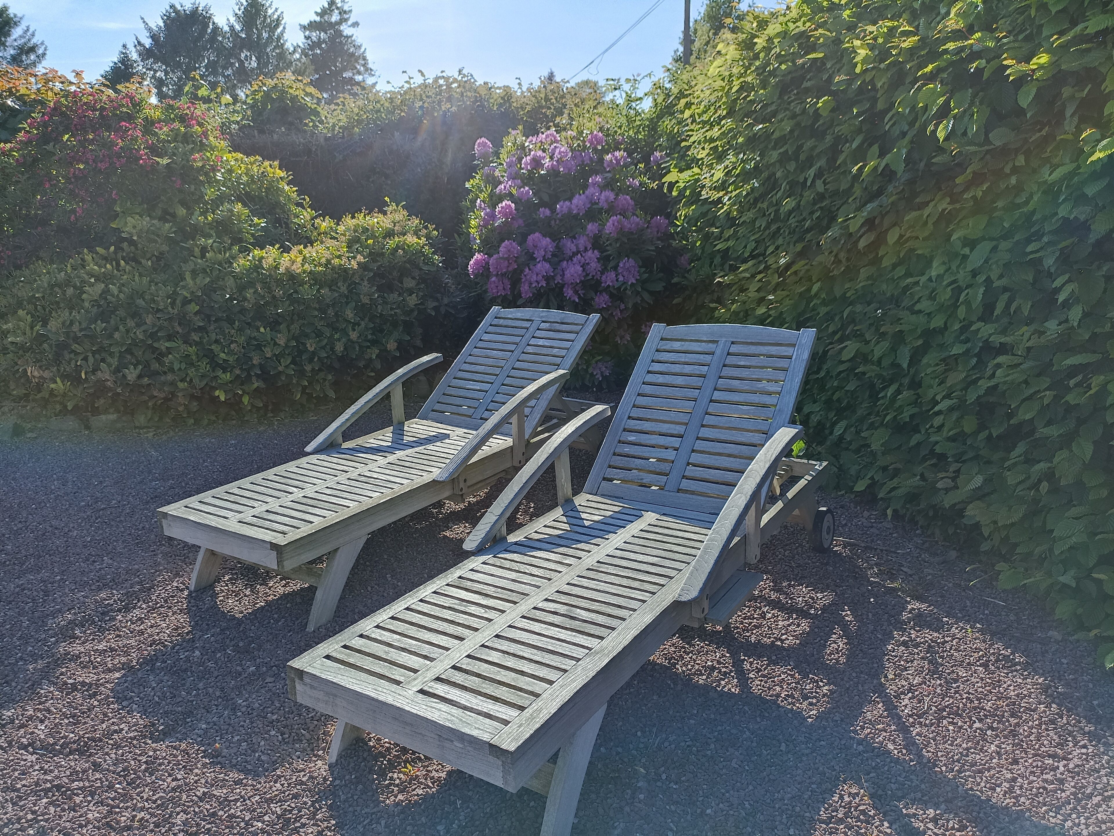Two wooden lounge chairs with metal frames, positioned on a gravel surface.
