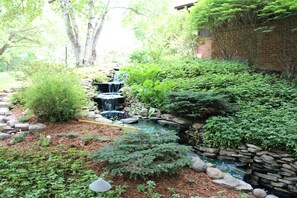 A garden with a small waterfall, surrounded by various plants and a stone wall. - Rivertown Inn (Gladwin)