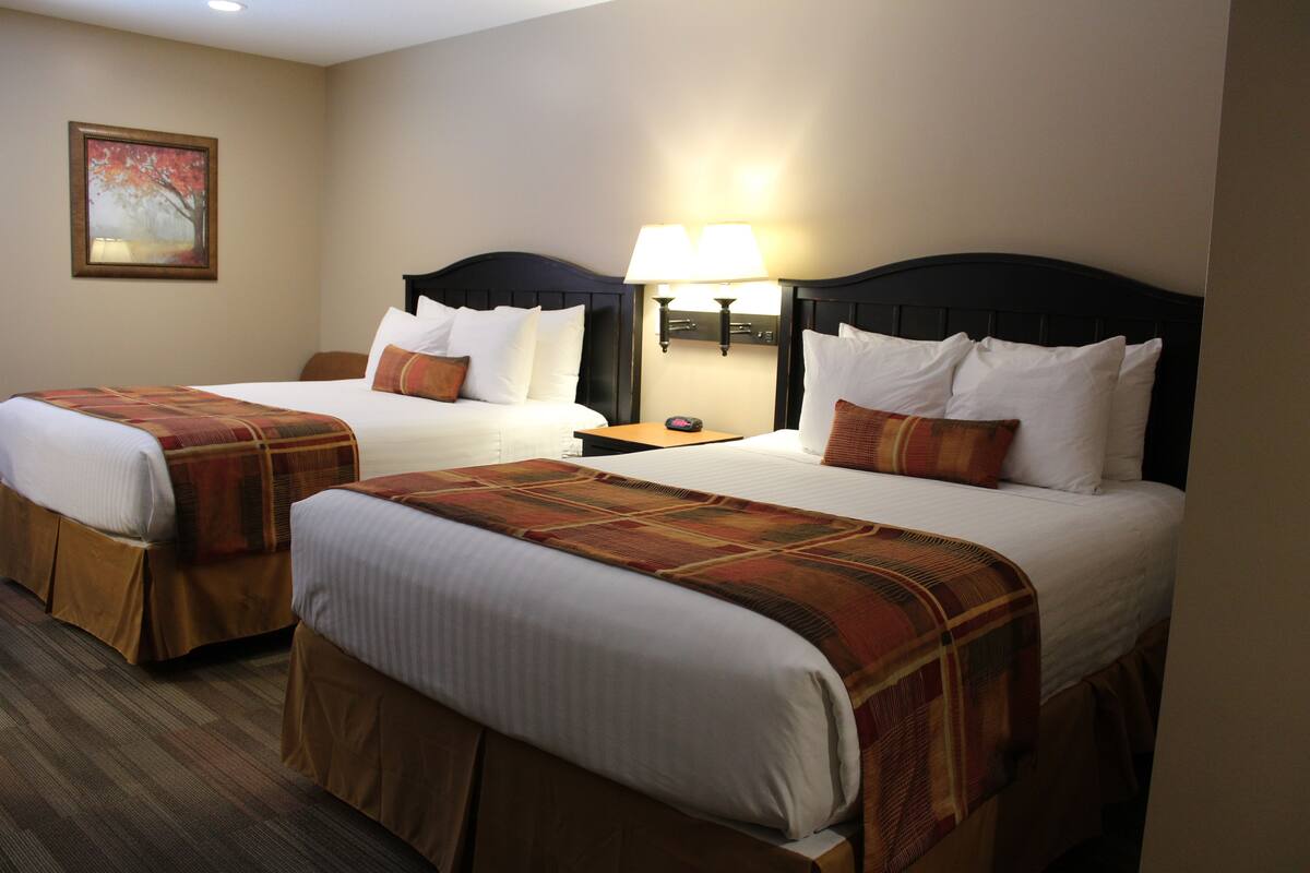 A hotel room with two beds, each with a headboard, a nightstand with a lamp, and a painting on the wall.