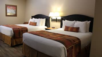 Habitación de hotel con dos camas, cada una con cabecera, mesita de noche con lámpara y un cuadro en la pared.