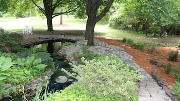 Un jardín con estanque, escalones de piedra y una zona ajardinada con sillas.