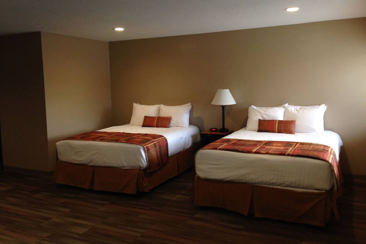 Two single beds with matching headboards and footboards, a bedside table with a lamp, and a wooden floor.