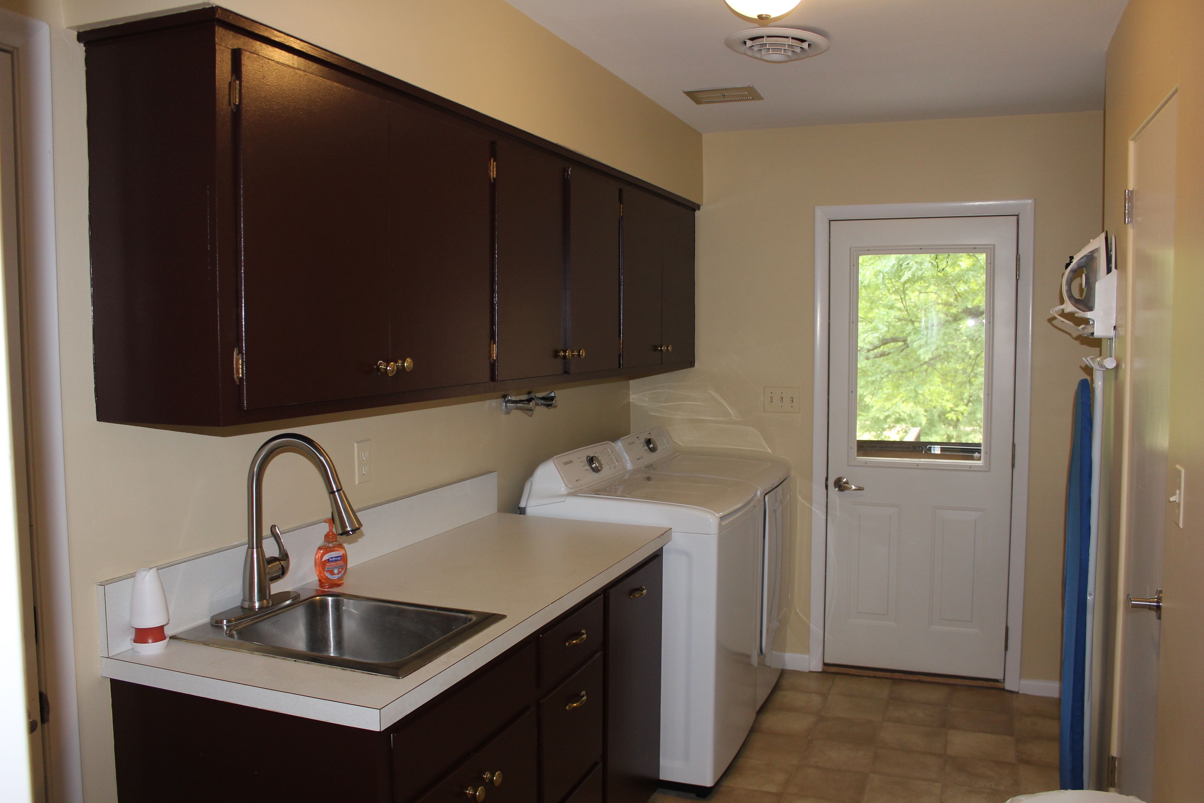 A laundry area with a washing machine, a sink, and dark wooden cabinets.