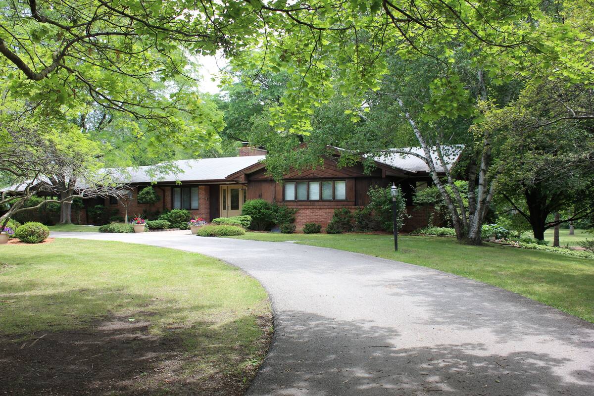 A house with a driveway leading to the front door, surrounded by trees and a well-maintained lawn.