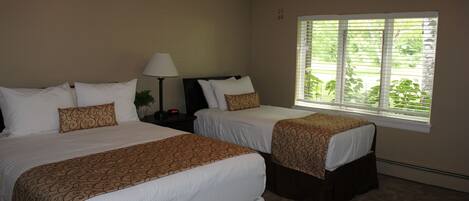 A hotel room with two beds, a ceiling fan, a window with blinds, and a nightstand with a lamp.