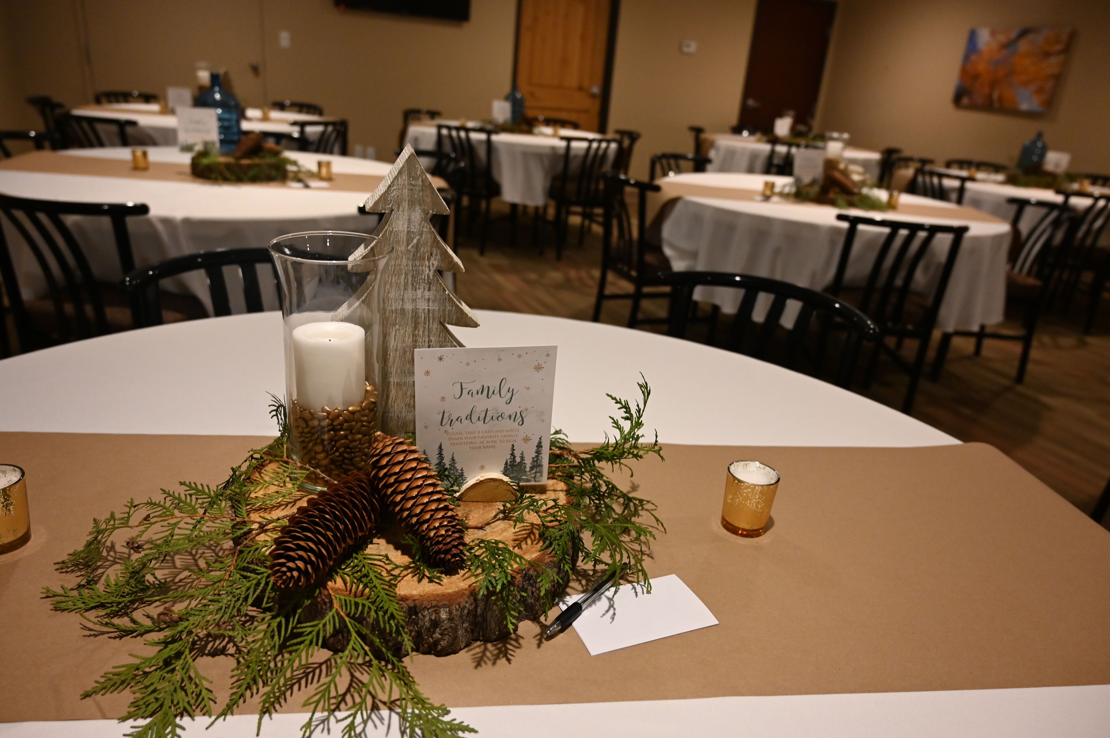 A dining table with a centerpiece featuring a pine cone, a small tree, and a card reading "Family Traditions."