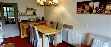 A cozy room with a wooden dining table, chairs, a sofa, and a radiator.