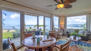 Um quarto espaçoso com uma mesa grande e cadeiras, um ventilador de teto e vista para o oceano.