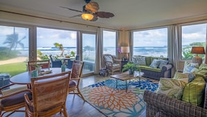 Quarto espaçoso com uma grande janela com vista para o mar, um ventilador de teto e uma área de jantar com móveis de vime.