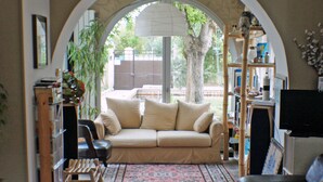 Un salon comprenant un canapé, une table basse et un téléviseur. Une grande fenêtre avec un arc en plein cintre donne sur l’extérieur.