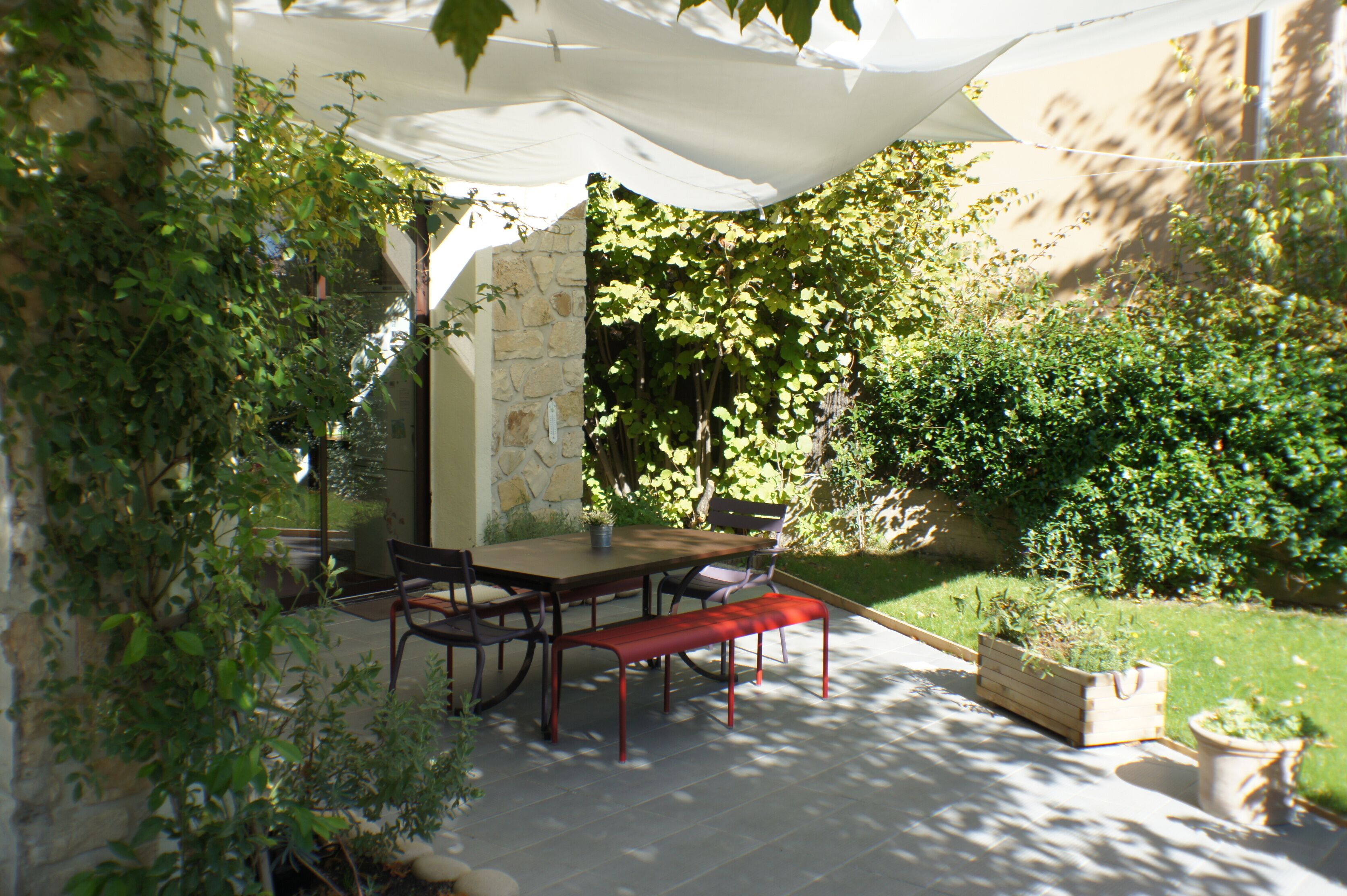 Eine Terrasse im Freien mit Tisch und Stühlen, umgeben von Grünpflanzen und einer Steinmauer.