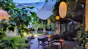 Un espace extérieur aménagé en terrasse, avec une table et des chaises, entouré de plantes en pot et doté d’un grand parasol pour créer de l’ombre.