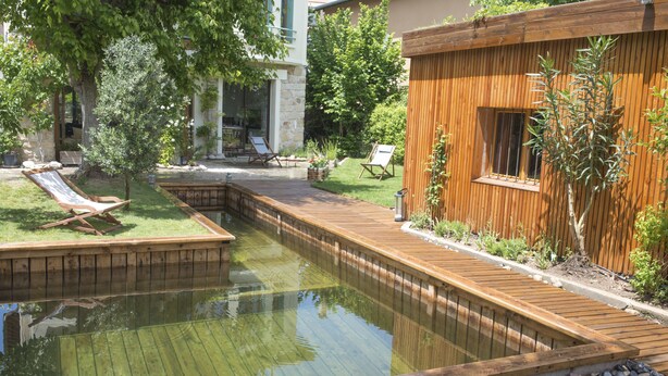 Une terrasse en bois avec un petit étang, entourée d’une clôture en bois et de verdure.