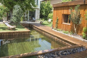 Eine Holzterrasse mit einem kleinen Teich, umgeben von einem Holzzaun und viel Grün.