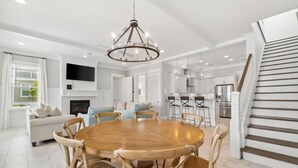 A spacious living area with a round wooden table and chairs, a chandelier, a fireplace, and a kitchen in the background. - Prime Location Near Community Pool | 6 Beach Bikes | Tram to Easy Beach Access (Santa Rosa Beach)
