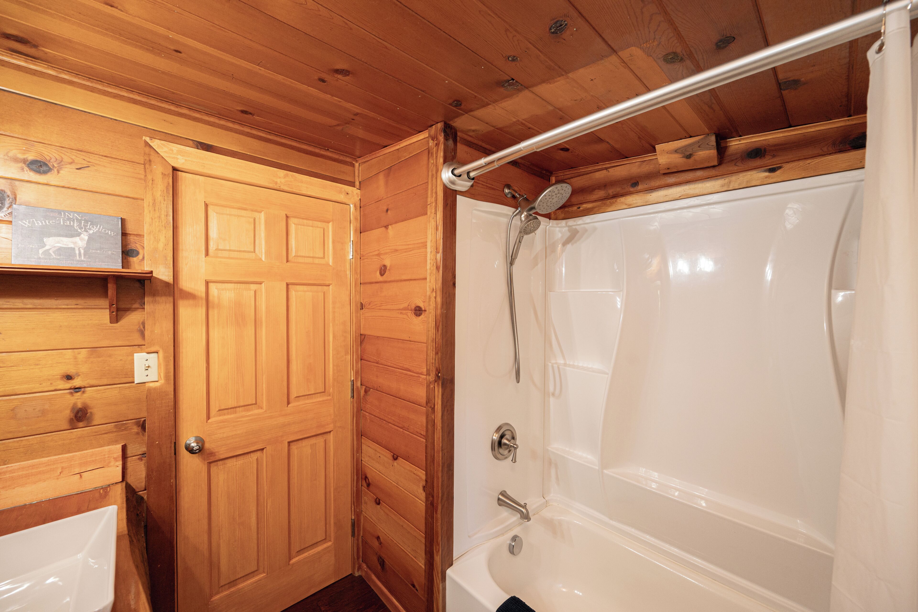 Un interior de madera con una bañera blanca, una puerta y una barra para cortina de ducha.
