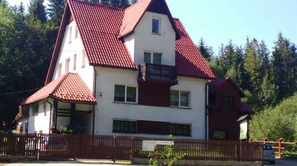 A two-story house with a red roof, white walls, and a wooden fence.