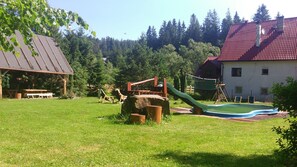 A playground with a slide and swings, a picnic table, and a house with a red roof.