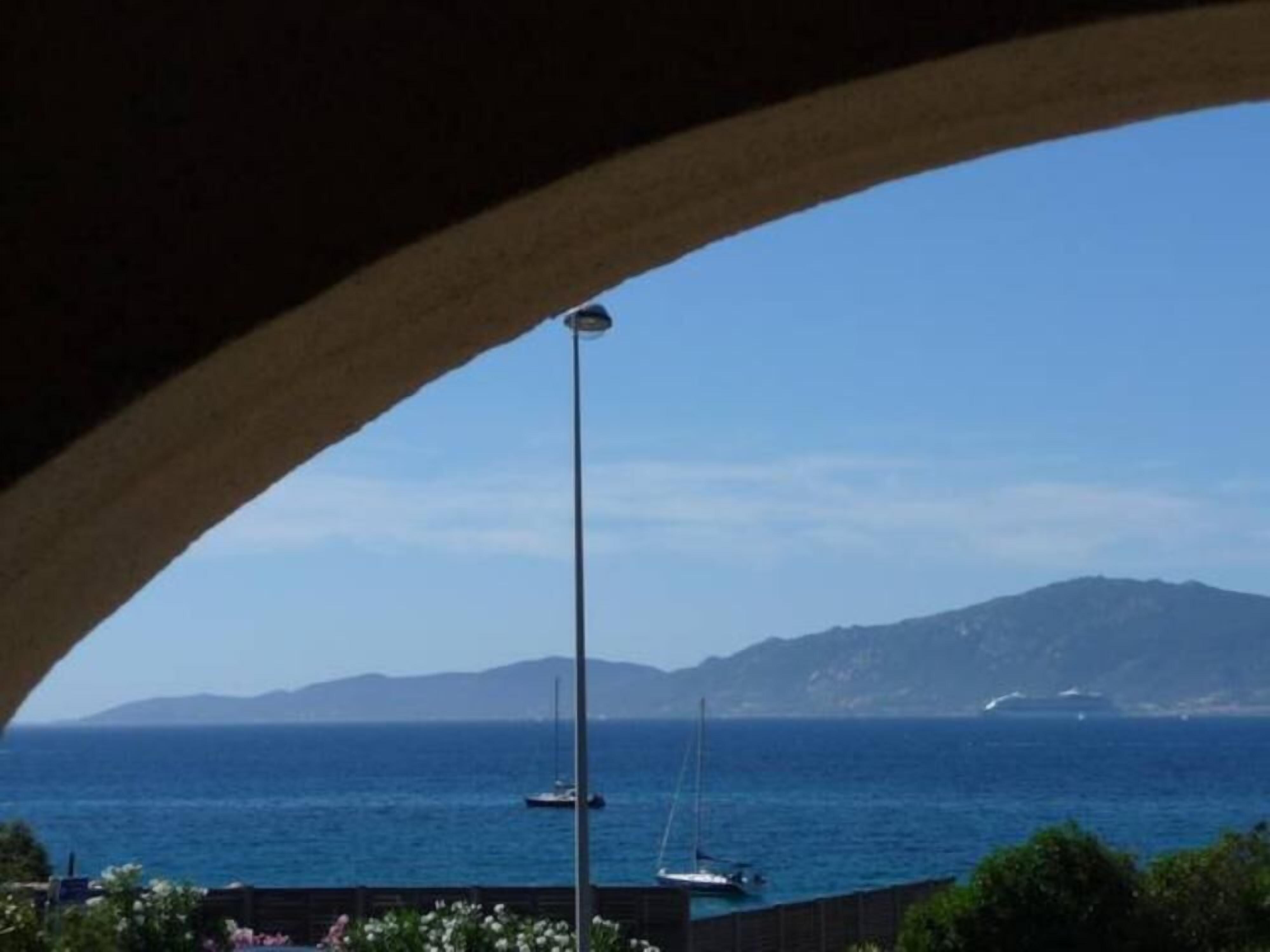 Blick aufs Meer durch ein Rundbogenfenster, mit Booten und Bergen in der Ferne.