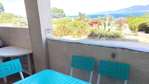 Een turquoise tafel met stoelen voor een muur, met uitzicht op een kustlandschap.