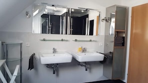 A modern bathroom with two sinks, a large mirror, and a glass shower enclosure.